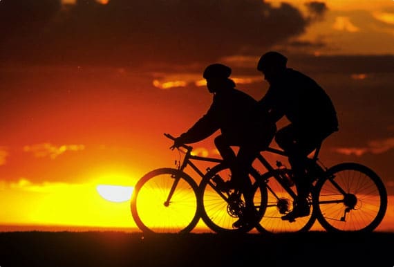 Two cyclist pedaling with a setting sun in the background.