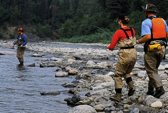 Fisherwoman reeling one in while man waits to net in the background and another man looks on.